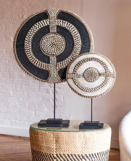 Two beaded ceremonial discs on stands, displayed on a woven stool in a contemporary interior