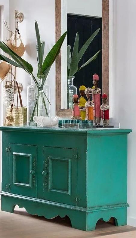 Namji dolls styled on a teal cabinet with tropical foliage in a contemporary collector's interior