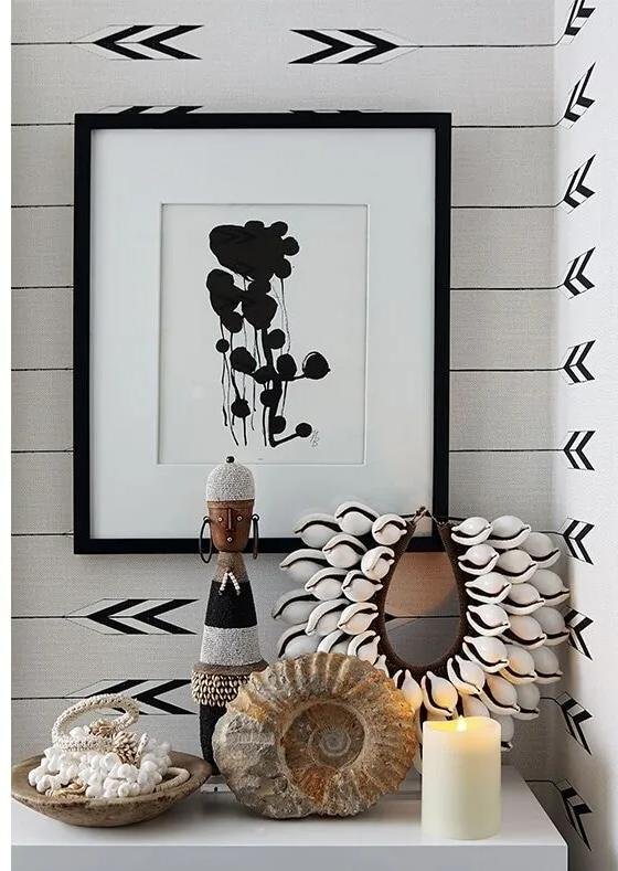 A Namji doll styled with cowrie jewellery, a fossil and candle in a monochrome interior