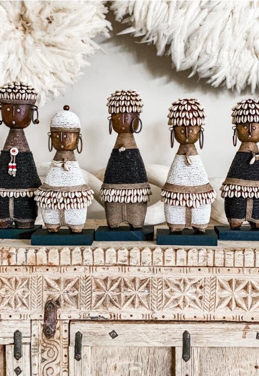 A collection of Namji dolls styled on a carved cabinet beneath feather wall hangings