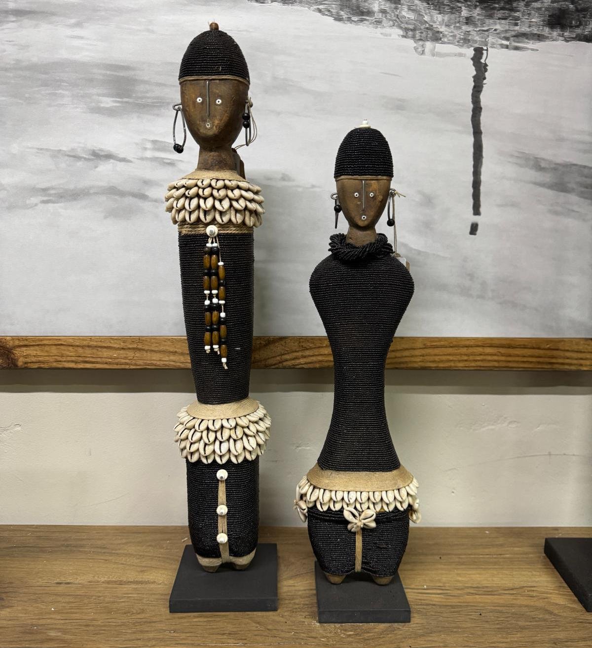 A pair of beaded Namji dolls with cowrie-shell adornment, displayed on a wooden console